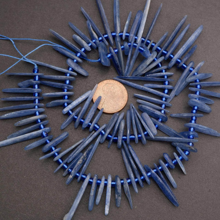Blue beaded circular necklace with a penny for scale on a brown background