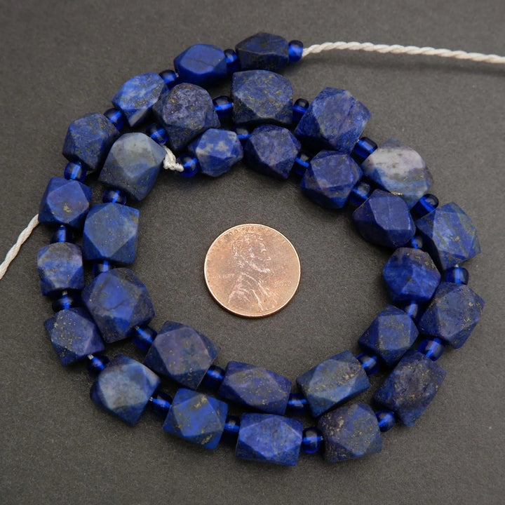 Blue faceted beads on a string with a penny for size comparison on a gray background