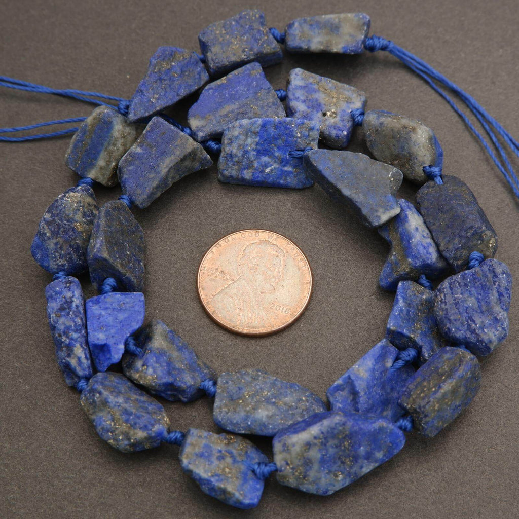 Lapis lazuli beads on a string with a penny for size comparison on a gray background