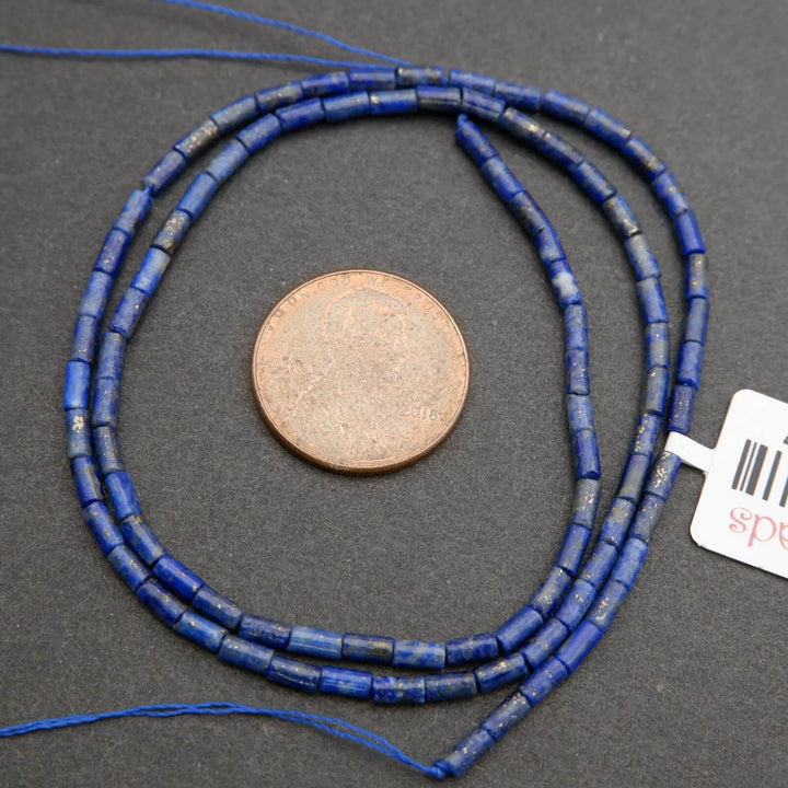 Blue beaded necklace with a penny for scale on a gray surface, with a brand tag visible.