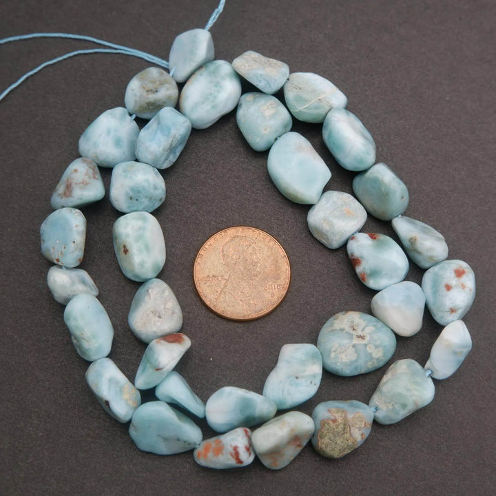 String of blue-green beads with a penny for size comparison on a dark background
