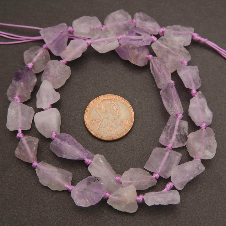 Necklace of pink amethyst beads with a penny for scale on a dark surface