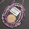 Three strands of purple and white beads with a coin underneath on a dark surface, accompanied by a label.