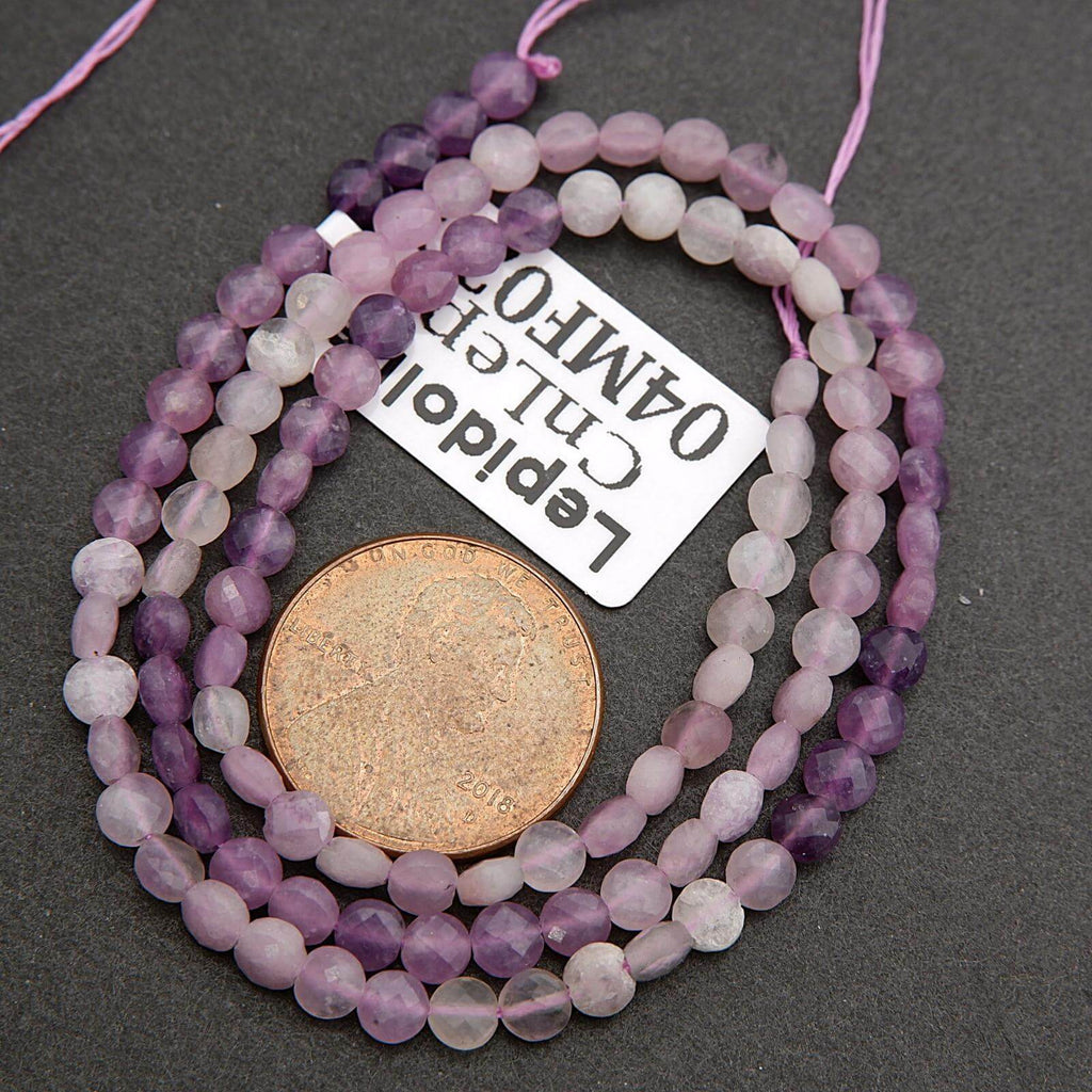 Three strands of purple and white beads with a coin underneath on a dark surface, accompanied by a label.