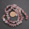 String of pink beads with a coin for scale on a gray background