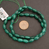 Green beads on a string with a coin for size comparison on a gray background