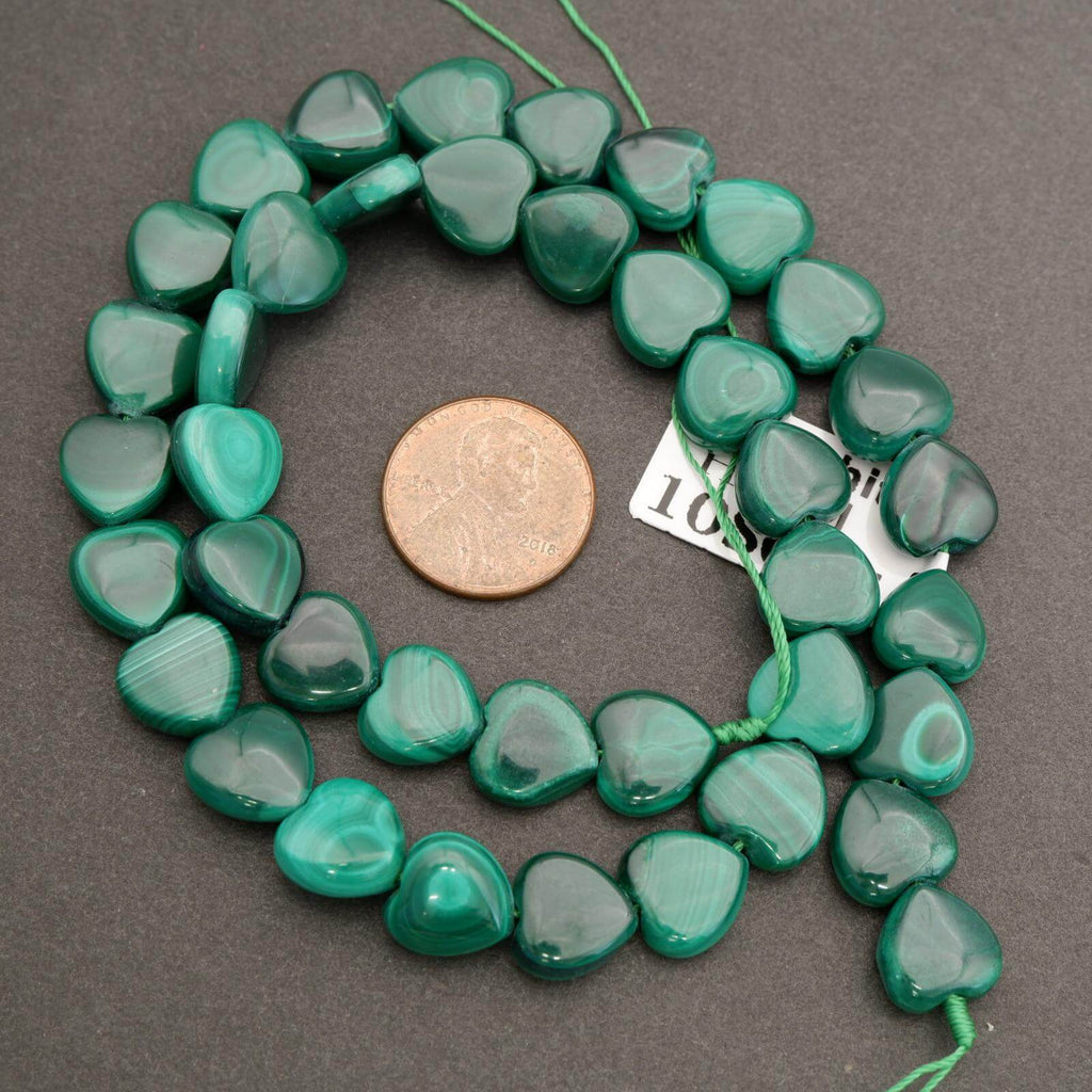 Green heart-shaped beads on a string with a coin for size comparison on a gray background