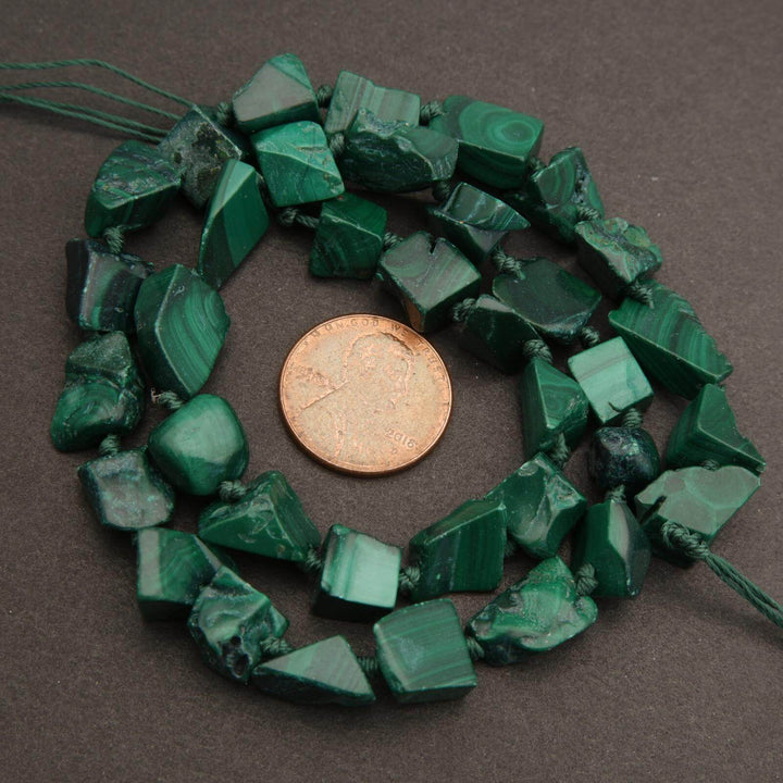 Green stone beads with a penny for scale on a brown background