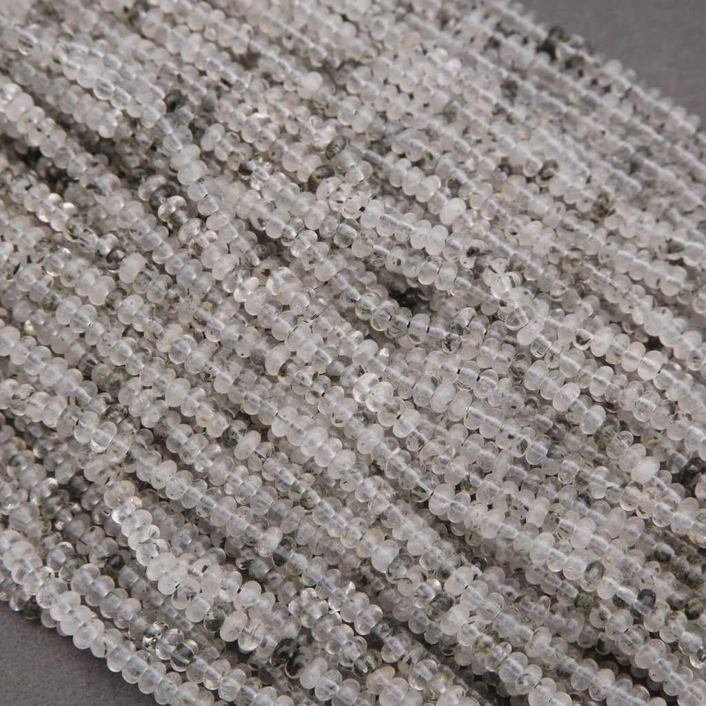 Close-up of clear quartz beads with black specks on a dark background.