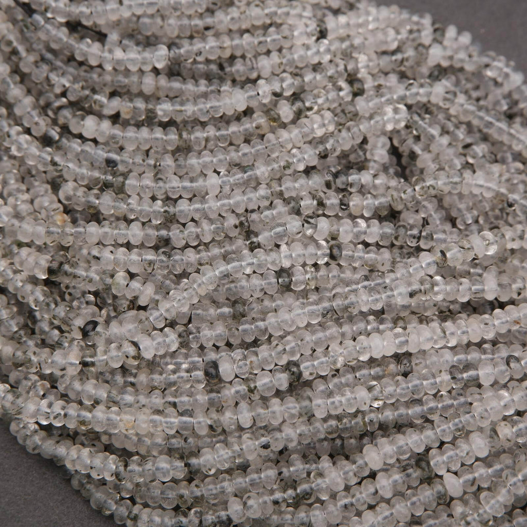 Close-up of clear quartz beads with black specks on a dark background.