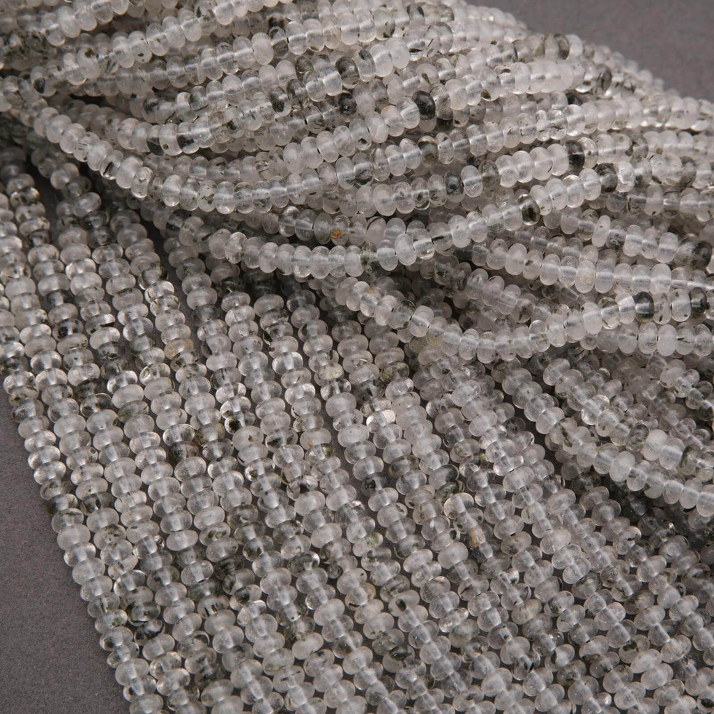 Close-up of clear quartz beads with black specks on a dark background.