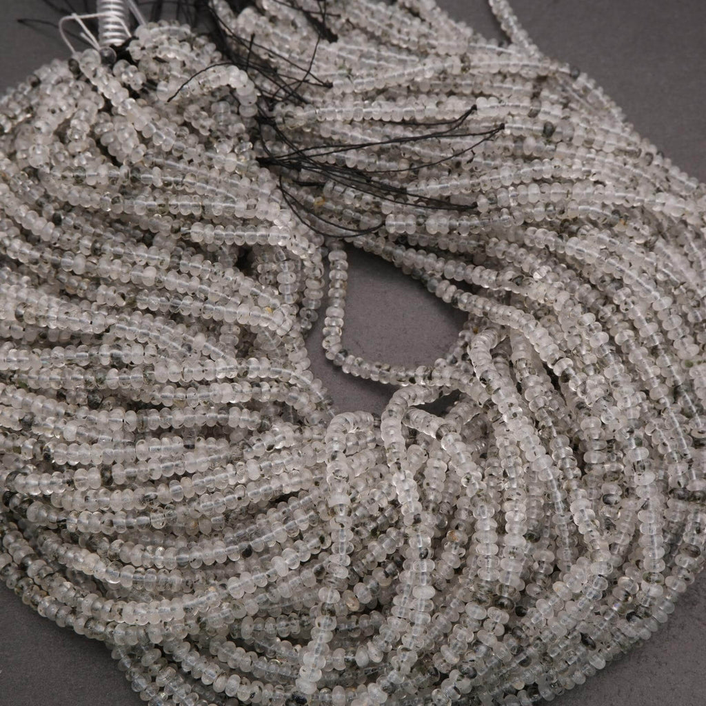 Close-up of clear quartz beads with black specks on a dark background.