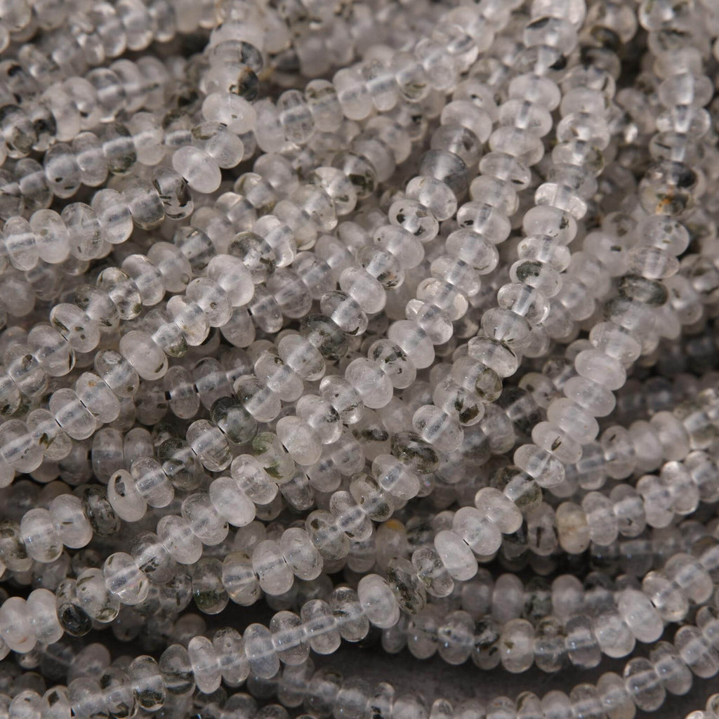Close-up of clear quartz beads with black specks on a dark background.