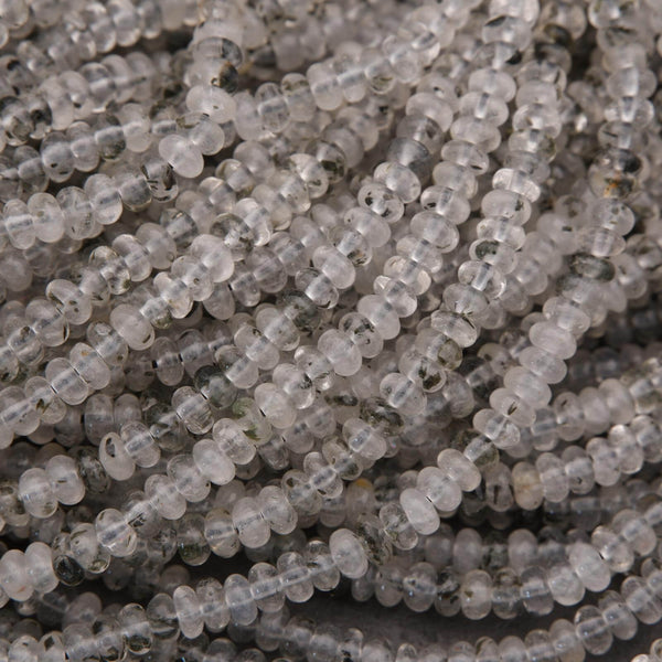 Close-up of clear quartz beads with black specks on a dark background.