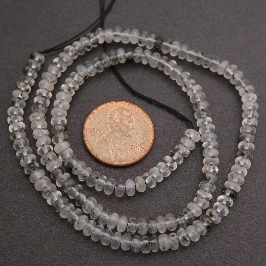 Close-up of clear quartz beads with black specks on a dark background.
