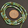 String of green and white beads with a penny for scale on a dark surface