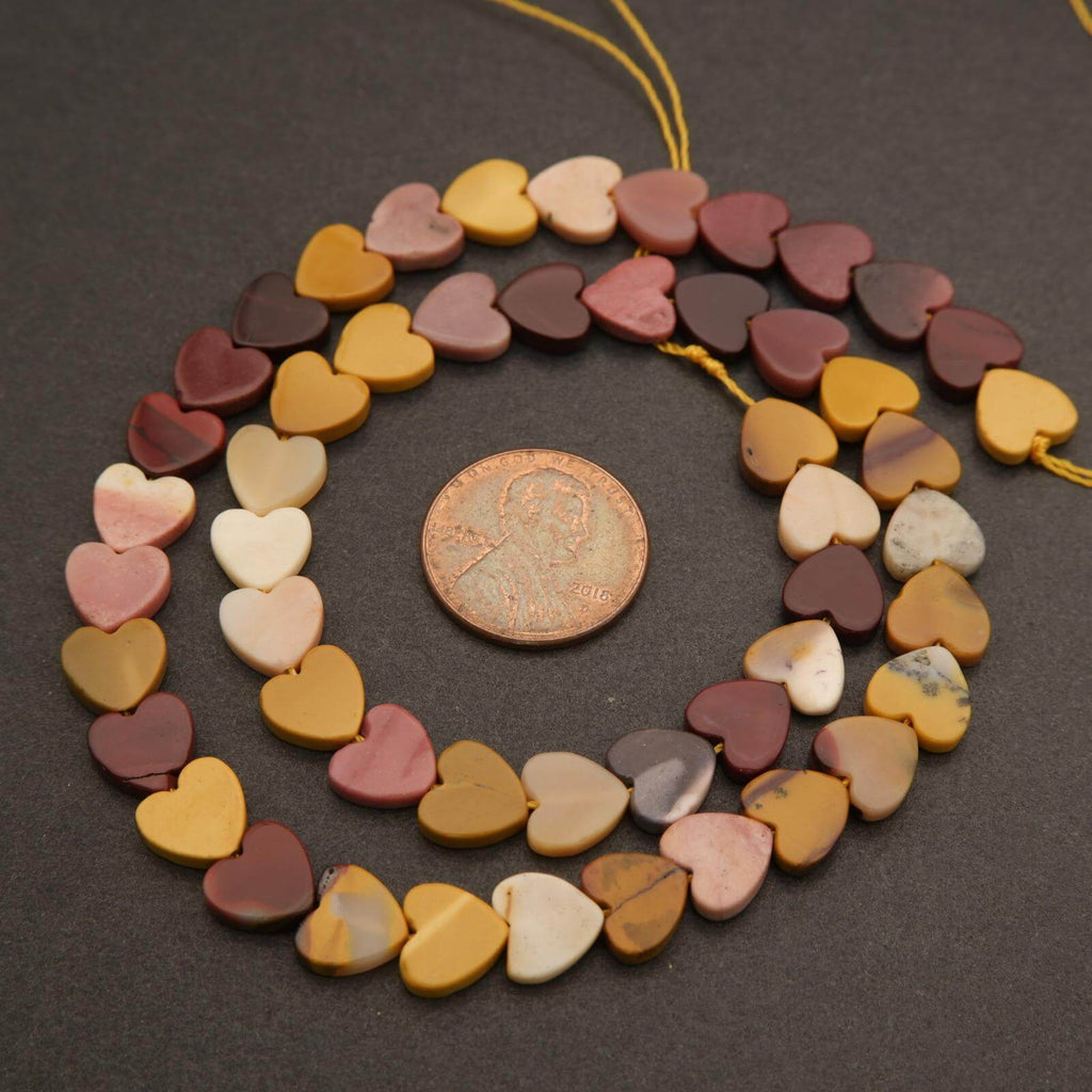 String of heart-shaped beads on a dark surface with a penny for scale.