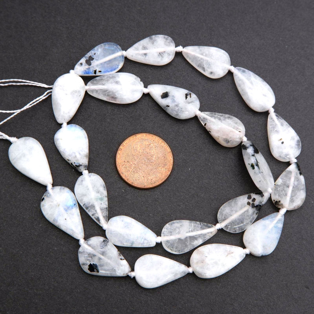 String of teardrop-shaped white beads with black spots on a dark surface, next to a penny for size comparison.