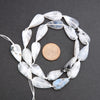 String of teardrop-shaped moonstone beads with a coin for scale on a dark surface