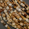 Close-up of mixed natural gemstone beads with smooth square shapes and organic color variation in neutral earth tones.