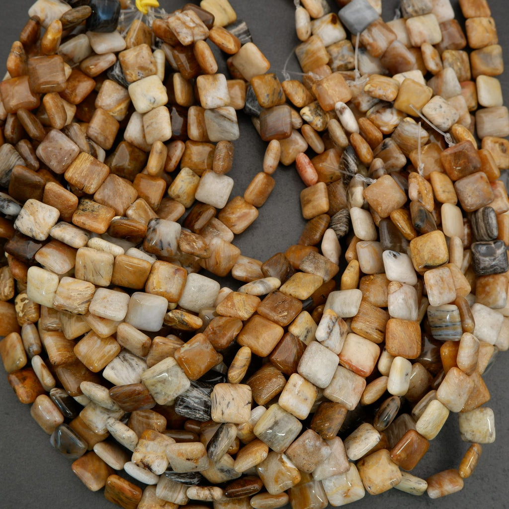 Assorted natural stone bead strands with square and rounded shapes displayed in warm neutral tones.