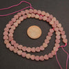 String of pink heart-shaped beads with a coin for size comparison on a dark surface