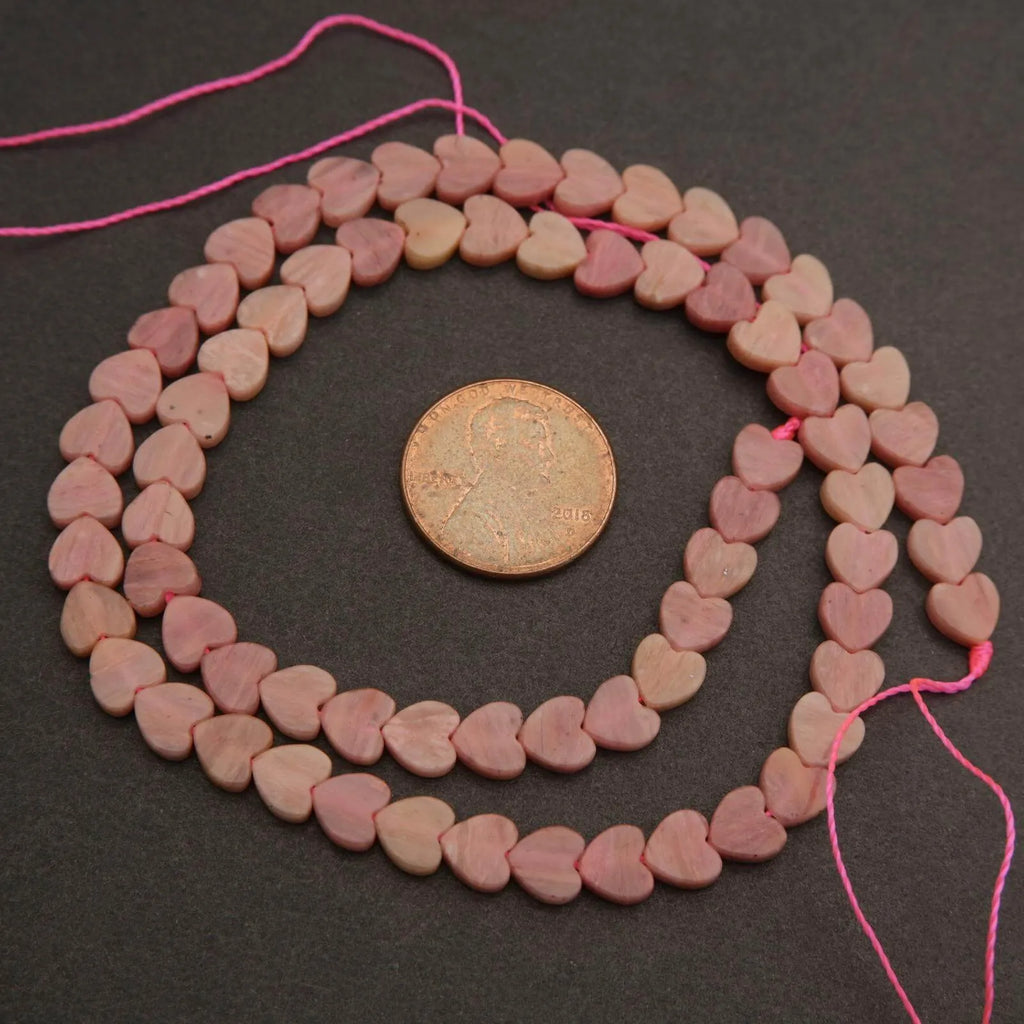 String of pink heart-shaped beads with a coin for size comparison on a dark surface