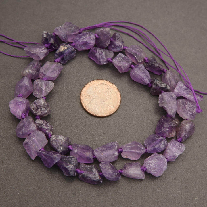 Necklace with purple amethyst beads next to a penny on a gray background