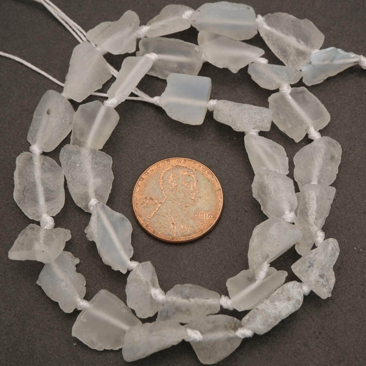 String of light gray beads with a penny for scale on a dark surface