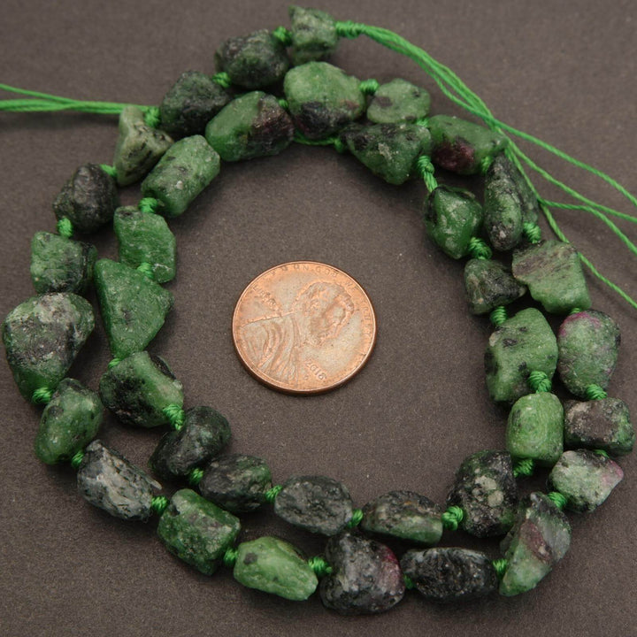 Green stone beads on a string with a penny for scale on a brown background