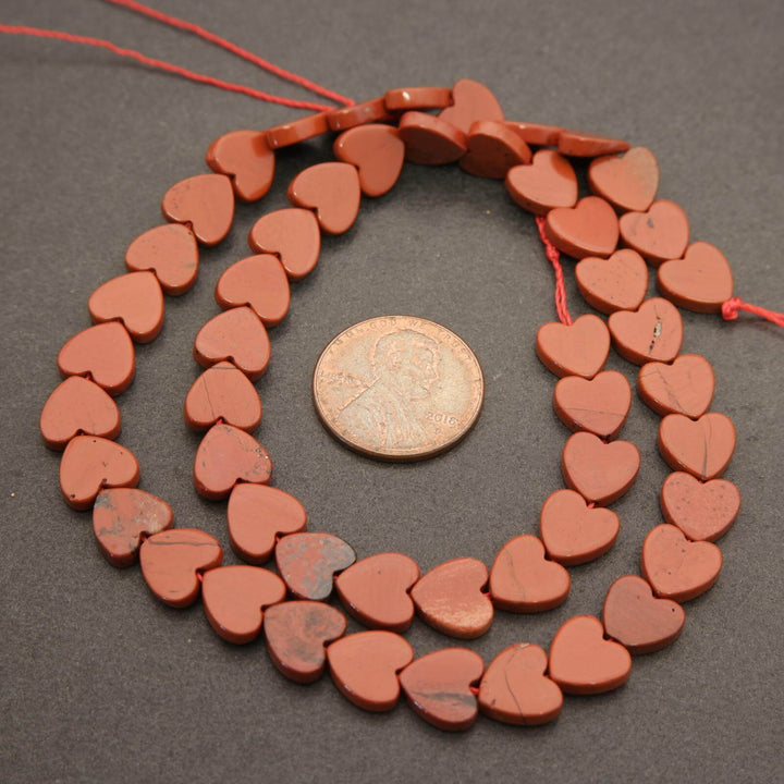 String of red heart-shaped beads with a coin for size comparison on a gray background