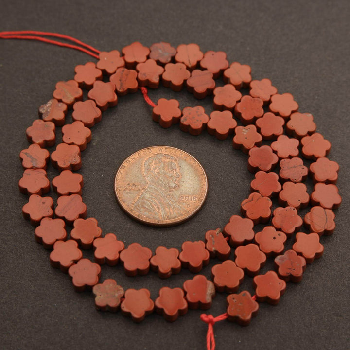 String of red flower-shaped beads with a coin for scale on a dark surface
