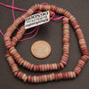 Necklace of pink and red beads with a coin for scale on a dark surface