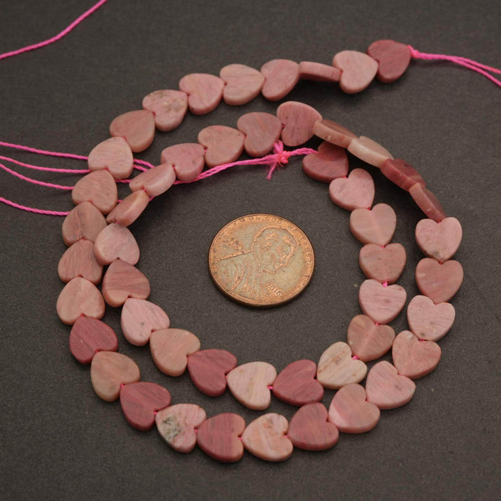 String of pink heart-shaped beads with a coin for scale on a dark surface