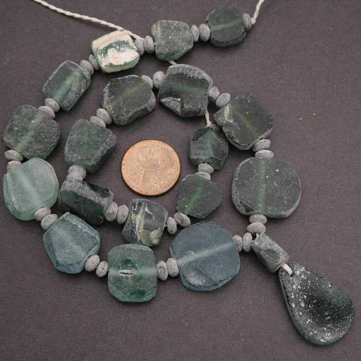 Necklace with green beads and a coin for scale on a dark background