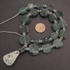 Necklace with green stone beads and a coin for scale on a dark surface
