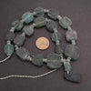 Necklace with green stone beads on a dark surface, with a coin for scale.