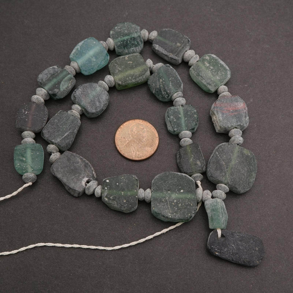 Necklace with green stone beads on a dark surface, with a coin for scale.