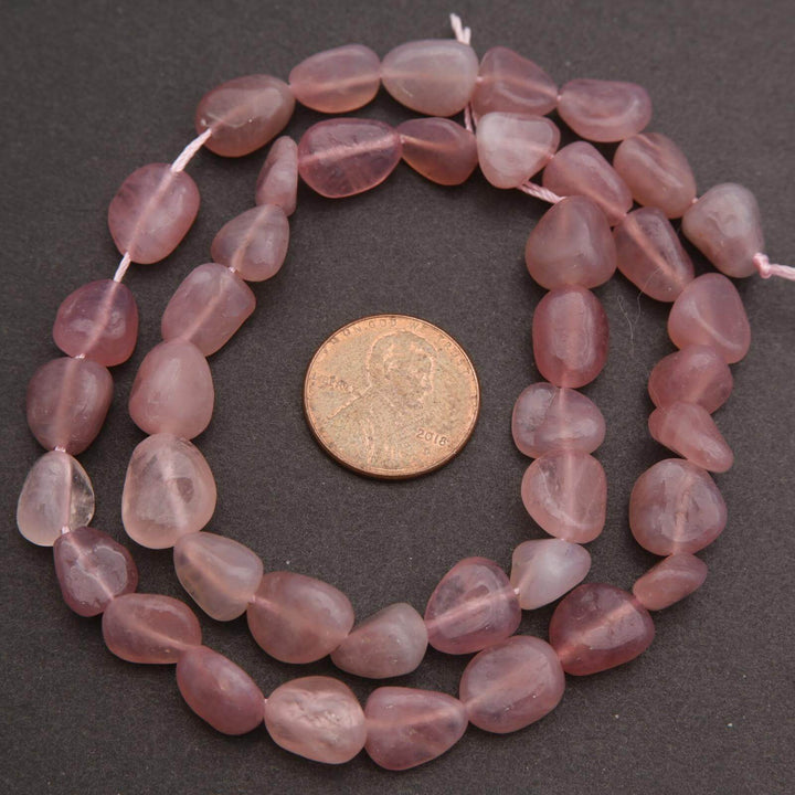 String of pink beads with a coin for size comparison on a dark surface