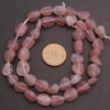 String of pink beads with a coin for size comparison on a dark surface