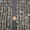 Close-up of raw labradorite beads with a penny for scale on a dark surface