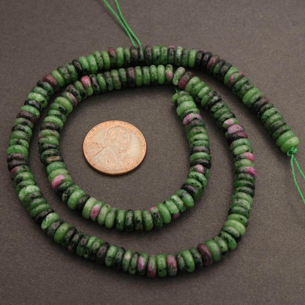 Green and purple bead necklace with a penny for scale on a gray background