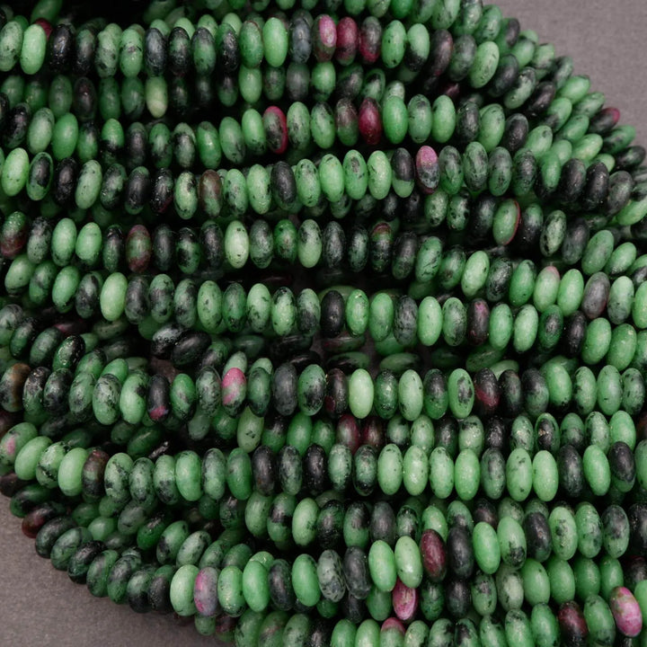 Close-up of polished ruby zoisite rondelle beads displaying mixed green, black matrix, and subtle pink ruby inclusions.