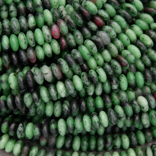 Macro close-up of ruby zoisite rondelle beads showing detailed surface texture, green feldspar, dark matrix, and ruby speckling.