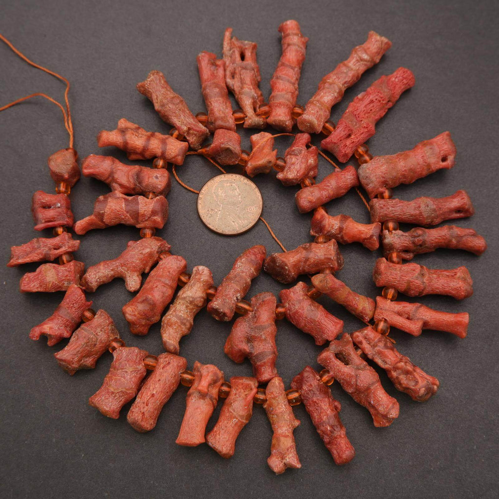 Red coral beads arranged in a circular pattern with a coin for scale on a dark surface