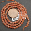 Necklace of orange beads with a penny for scale on a dark surface