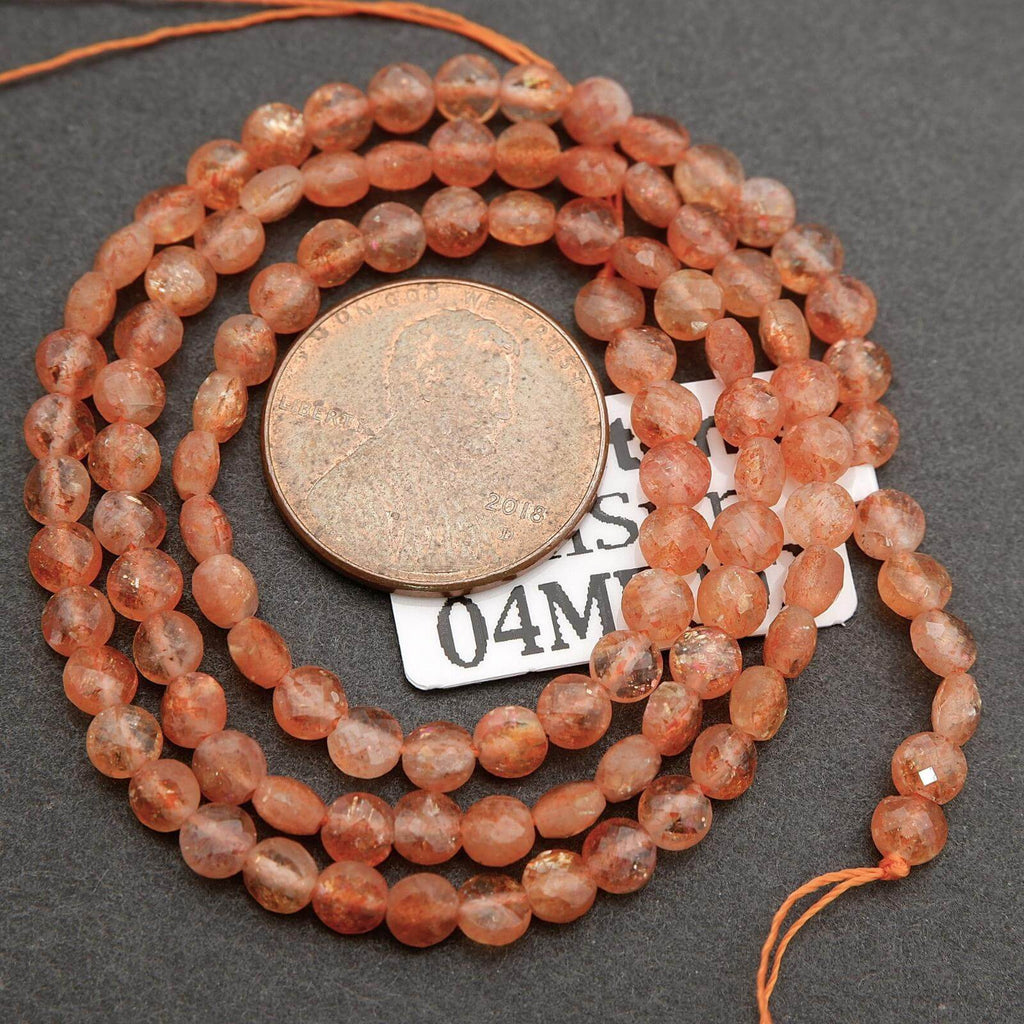 Necklace of orange beads with a penny for scale on a dark surface