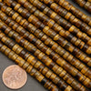 Polished tiger’s eye heishi beads in golden brown and bronze tones displayed beside a penny for scale.