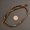 Beaded necklace with brown and black beads on a gray surface, next to a penny for scale.