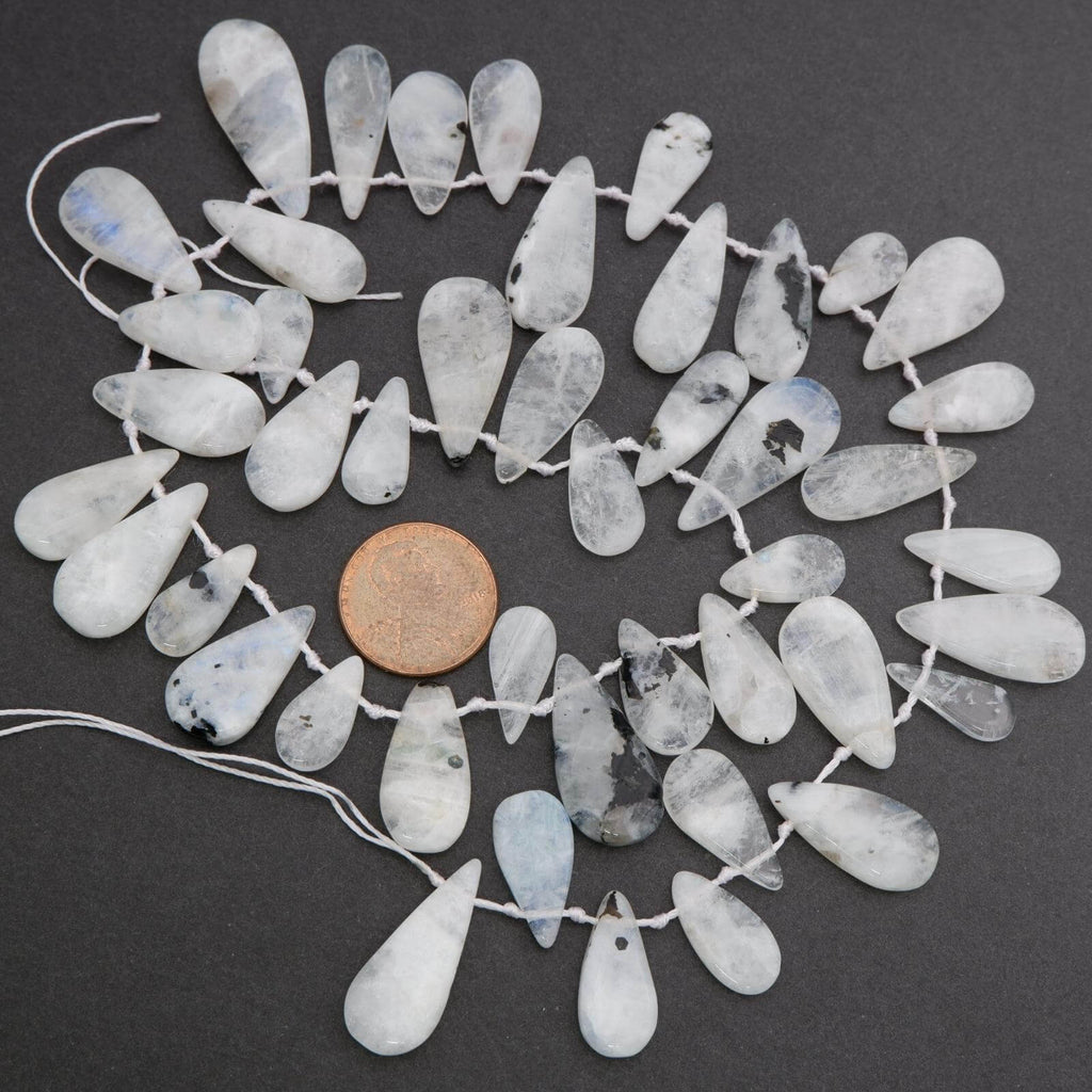 String of teardrop-shaped white beads with a penny for scale on a dark background